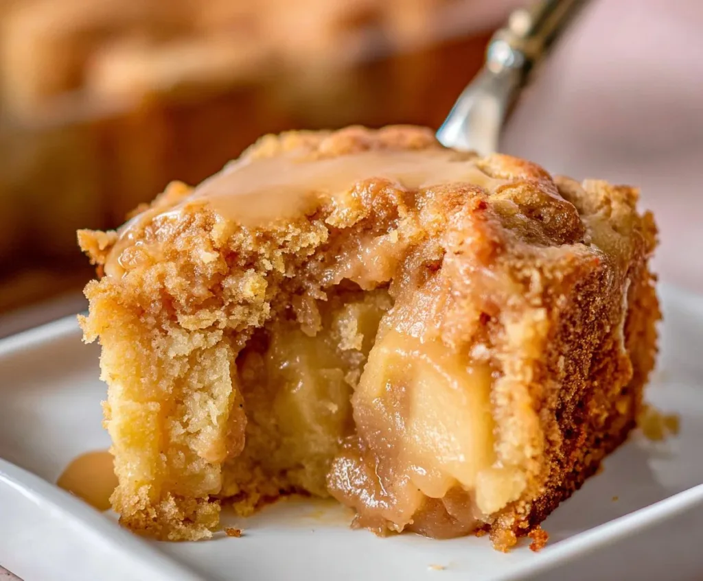 Slice of homemade Apple Dapple Cake on a plate with apples and cinnamon